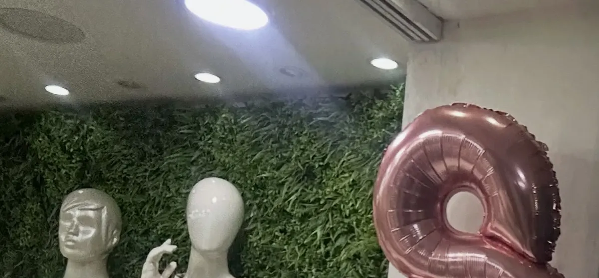 Interior da loja San Maria: manequins vestidos diante de uma parede verde e o balão dourado dos 8 anos.